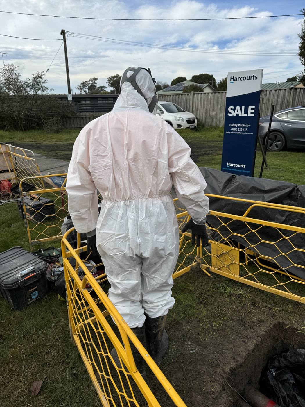 Worker in disposable coveralls and respirator inside a fenced work zone