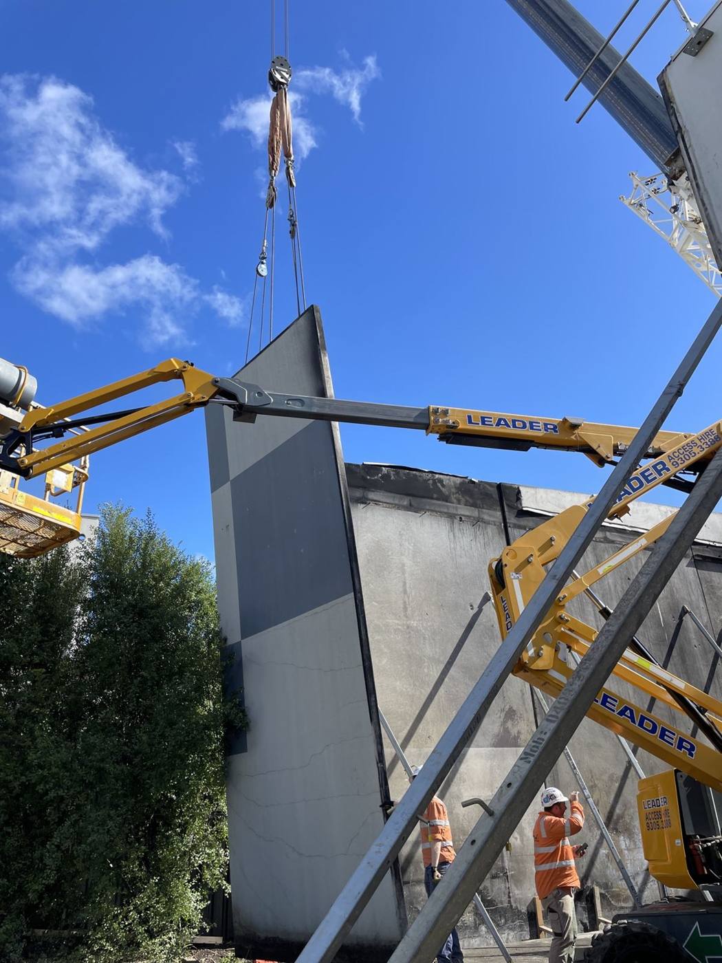 Precast concrete panel being lifted into place by crane, with elevated work platforms on site